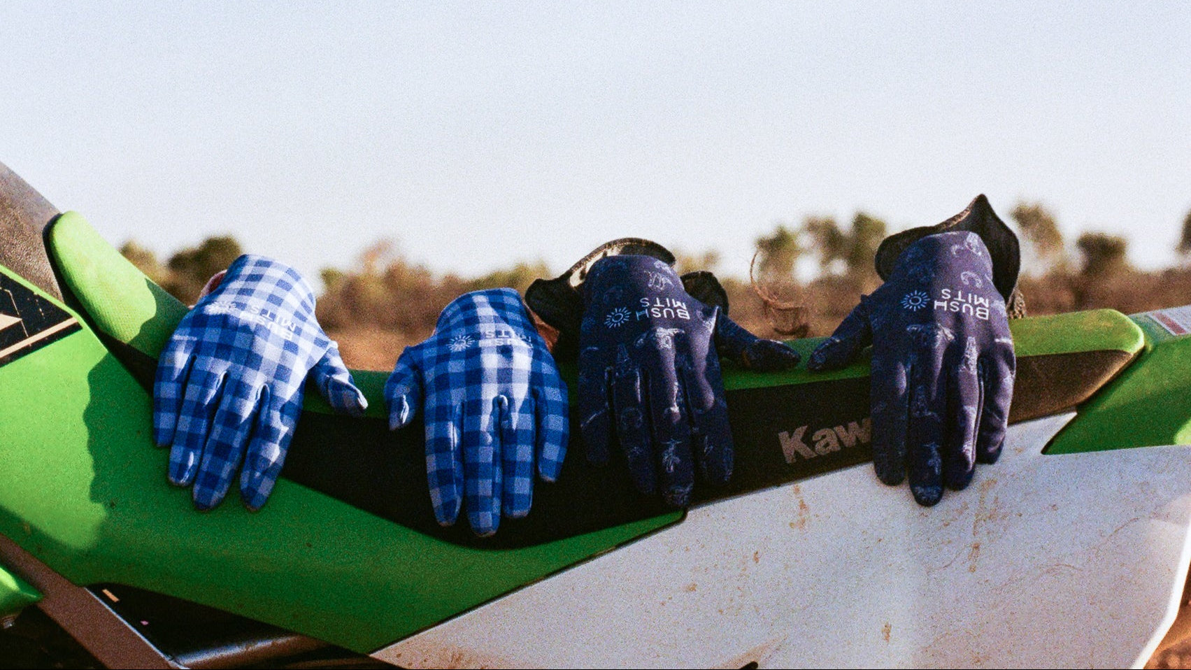 Close-up of hands wearing blue and black gloves on a green vehicle against a clear sky.